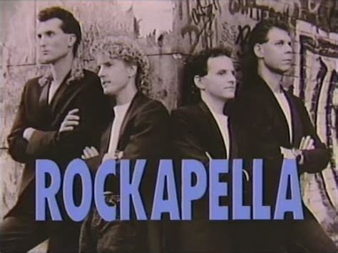 Grayscale image of (from left to right) Sean Altman, Scott Leonard, Elliot Kerman, and Barry Carl leaning against a graphitti covered stone wall, wearing black suit coats and white undershirts. They all have their arms crossed and are looking cool as hell. The word 'Rockapella' appears in all caps below them.